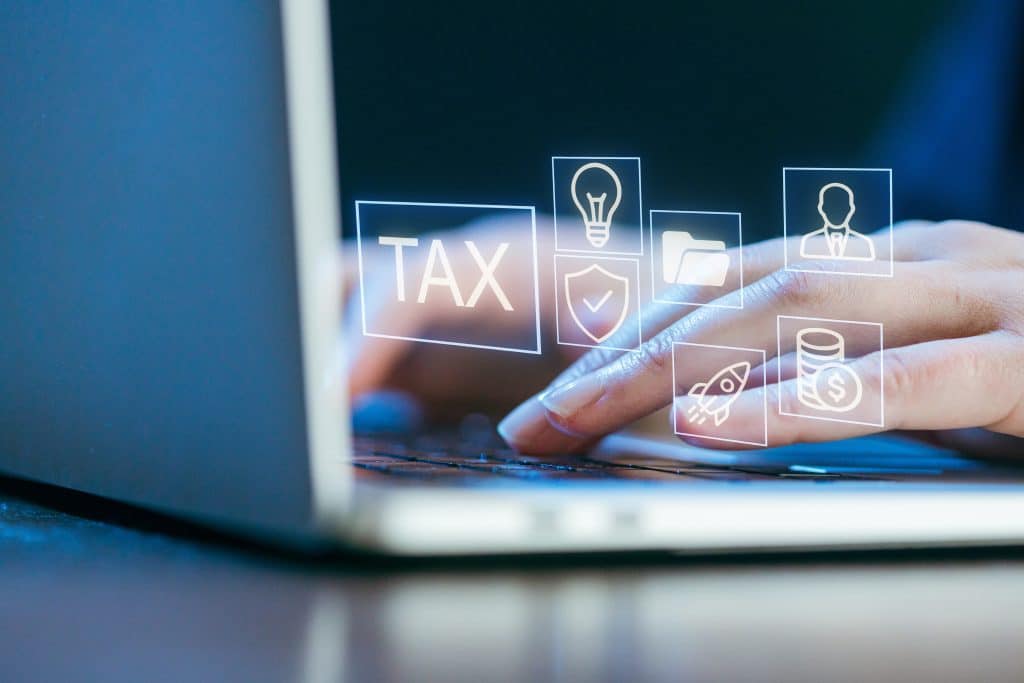 パソコンで会計ソフトに入力している女性の手元とTAXやお金のアイコン。