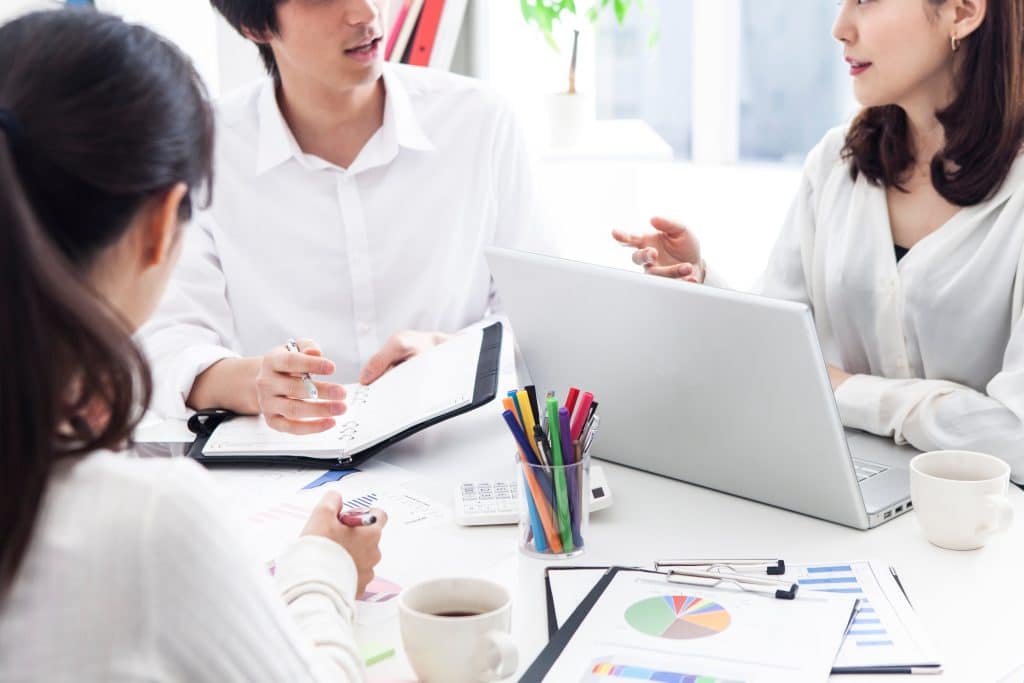 販促・ブランディング戦略をデータ資料とノートPCで検討する3人のミーティング